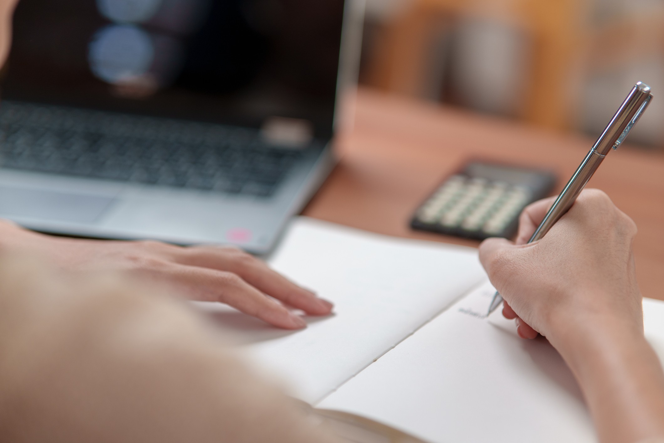 sobre a mesa notebook, calculadora e uma pessoa anotando em um papel